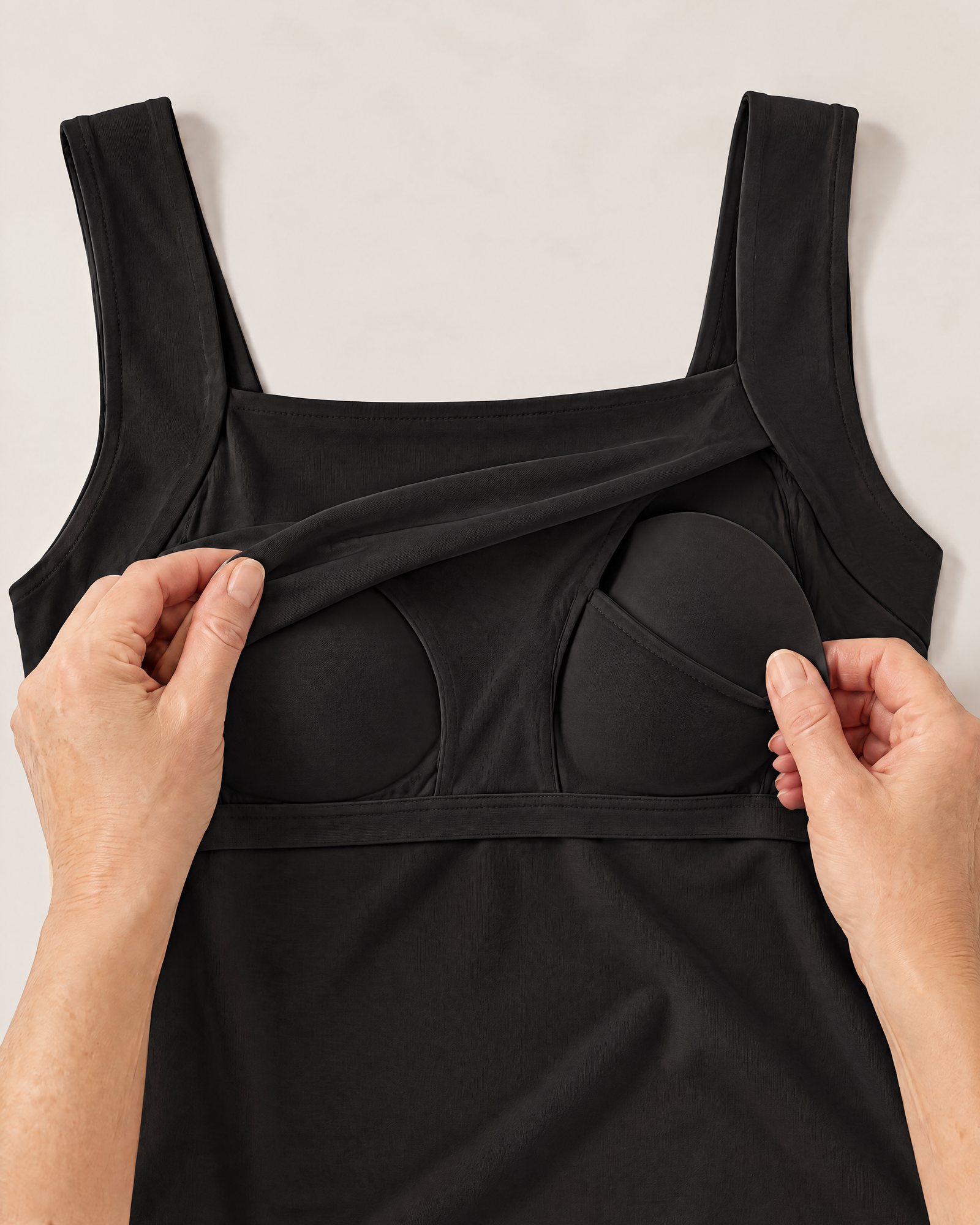 Hands holding the neckline of the Comfort Tank, Black open to show the inner layer and a padded cup in its pocket