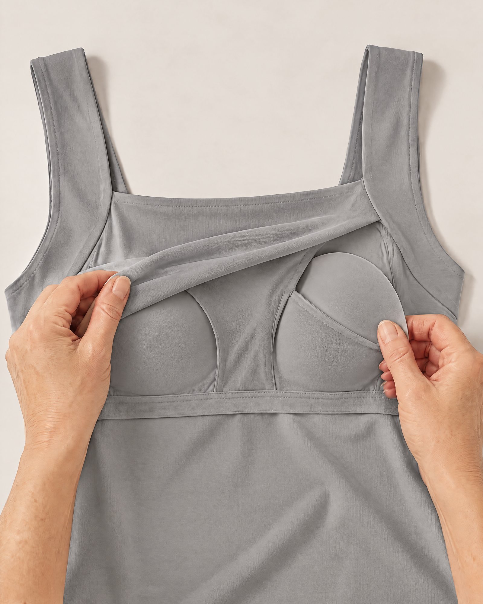 Hands holding the neckline of the Comfort Tank, Gray open to show the inner layer and a padded cup in its pocket